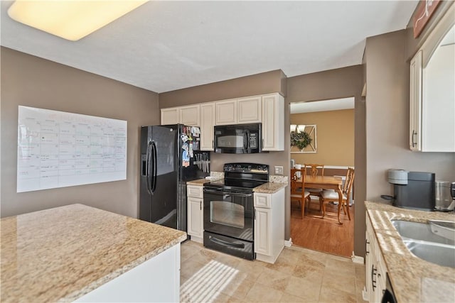 kitchen featuring light stone counters, white cabinets, black appliances, and a sink