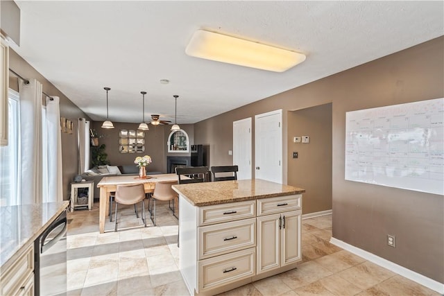 kitchen with decorative light fixtures, open floor plan, light stone counters, a fireplace, and cream cabinets