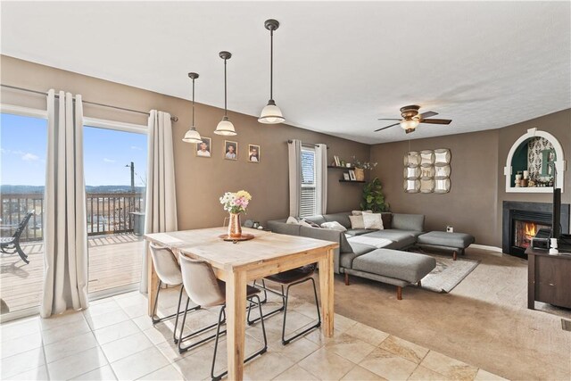 dining area featuring light colored carpet, a ceiling fan, and a lit fireplace