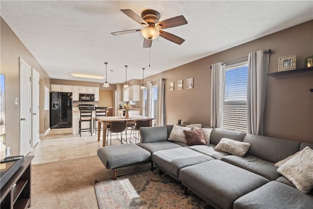 living area featuring light carpet, light tile patterned floors, a textured ceiling, and a ceiling fan