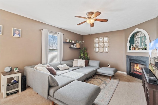 living room featuring a glass covered fireplace, light colored carpet, baseboards, and a ceiling fan