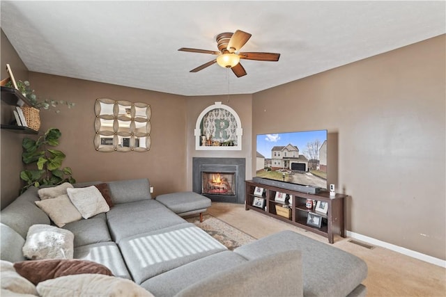 living room featuring visible vents, a ceiling fan, a lit fireplace, carpet, and baseboards