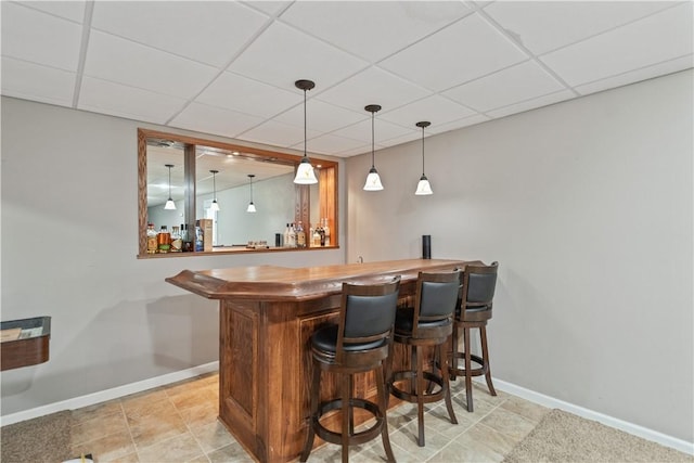 bar featuring decorative light fixtures, a bar, a paneled ceiling, and baseboards