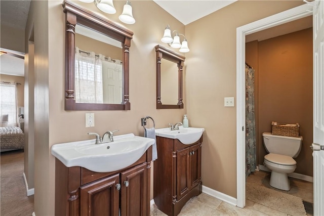 bathroom with toilet, two vanities, baseboards, and a sink