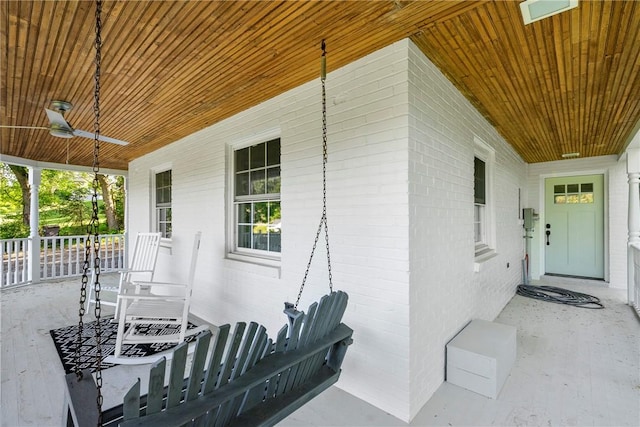 doorway to property with a porch, a ceiling fan, and brick siding