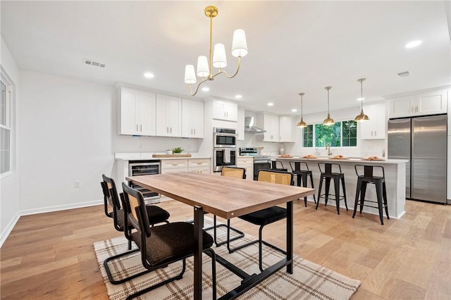 dining room with light wood-type flooring, recessed lighting, wine cooler, an inviting chandelier, and baseboards