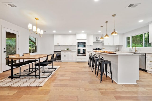 kitchen featuring visible vents, stainless steel appliances, wine cooler, white cabinetry, and wall chimney range hood