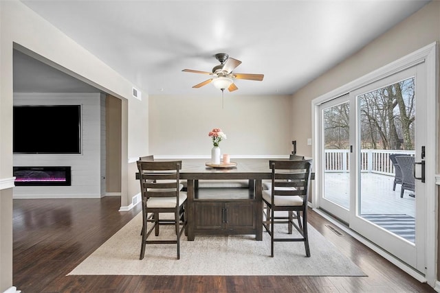 dining space with a ceiling fan, wood finished floors, visible vents, baseboards, and a glass covered fireplace