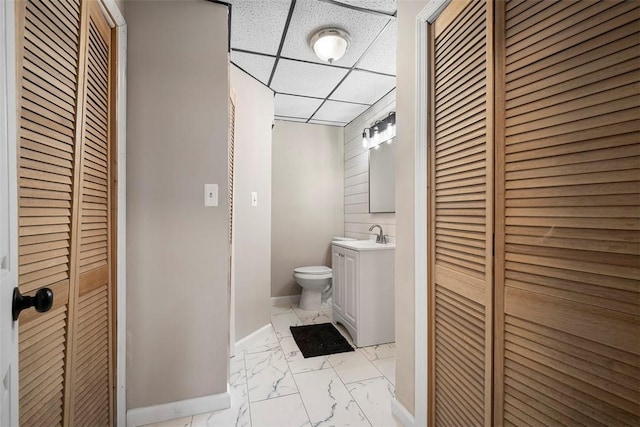 bathroom featuring toilet, marble finish floor, a drop ceiling, a closet, and vanity