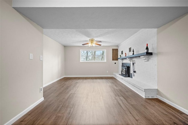 unfurnished living room featuring a ceiling fan, baseboards, dark wood finished floors, a wood stove, and a textured ceiling