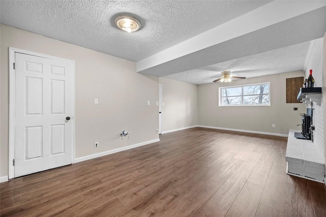 unfurnished living room featuring dark wood finished floors, a textured ceiling, baseboards, and a ceiling fan