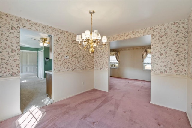 unfurnished dining area featuring a wainscoted wall, ceiling fan with notable chandelier, carpet flooring, and wallpapered walls