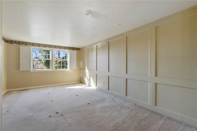 unfurnished room featuring baseboards, light colored carpet, and a decorative wall