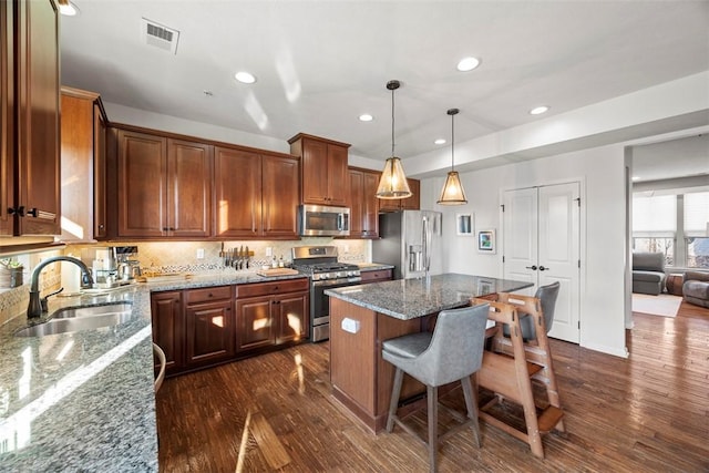 kitchen with visible vents, a sink, dark wood finished floors, stainless steel appliances, and stone counters