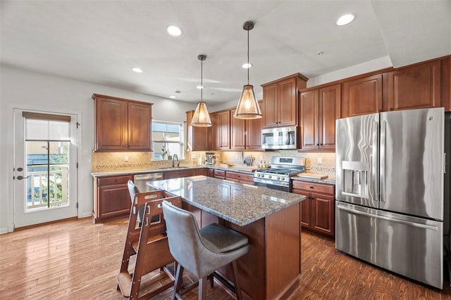 kitchen featuring dark stone countertops, a kitchen island, dark wood finished floors, a sink, and appliances with stainless steel finishes