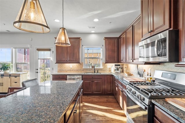 kitchen with visible vents, dark wood-type flooring, a sink, stainless steel appliances, and decorative backsplash