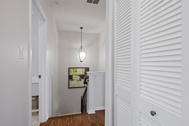 hallway with an upstairs landing, visible vents, dark wood-type flooring, and baseboards