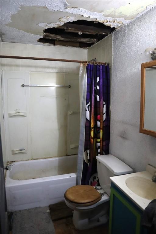 full bathroom with vanity, shower / bath combination with curtain, toilet, and a textured wall