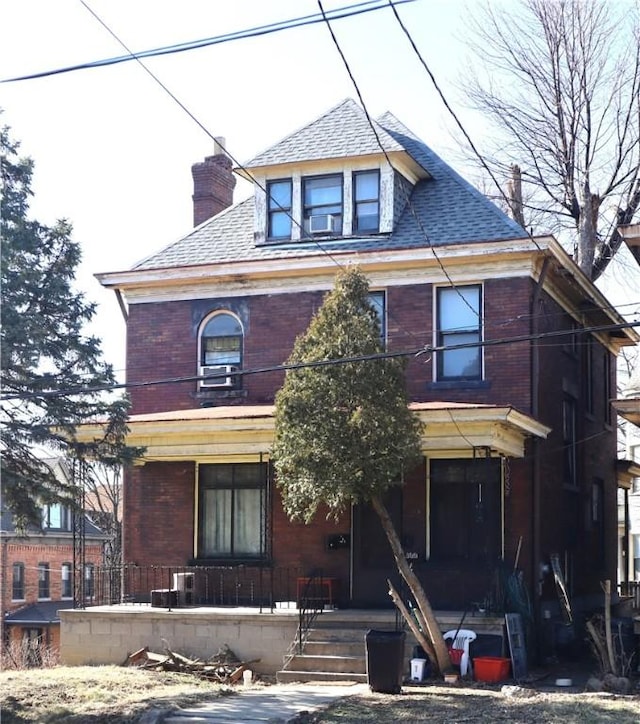 american foursquare style home featuring brick siding, covered porch, a chimney, and roof with shingles