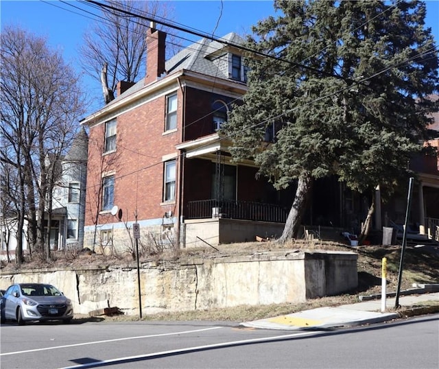 view of property exterior featuring covered porch, brick siding, and a chimney