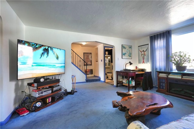 living area with a textured ceiling, stairway, arched walkways, carpet flooring, and baseboards