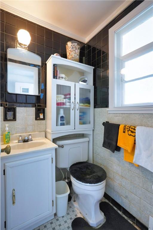 half bathroom featuring toilet, tile walls, and vanity