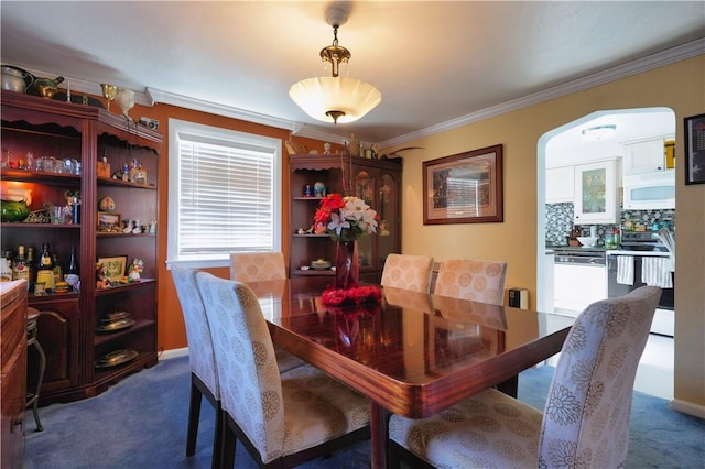 dining space with arched walkways, dark colored carpet, and ornamental molding