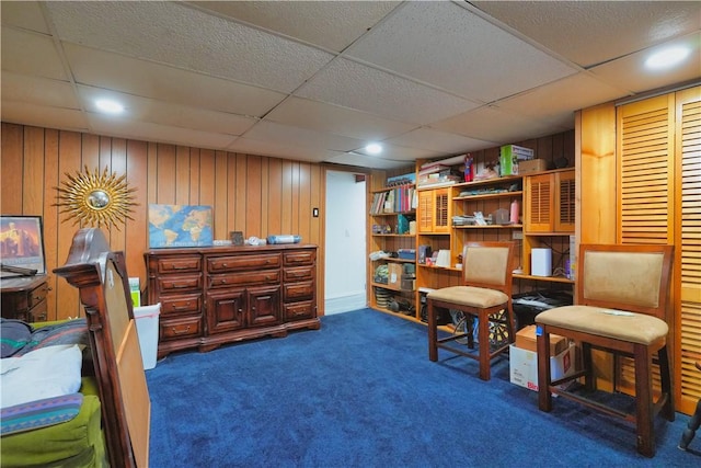 sitting room with a drop ceiling, wood walls, and dark carpet