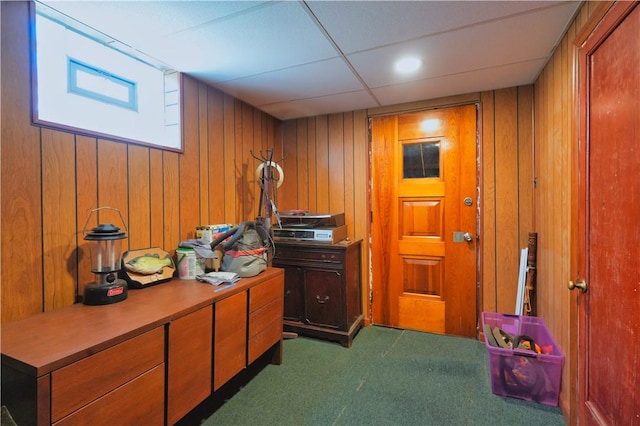 interior space featuring a paneled ceiling, dark colored carpet, and wood walls