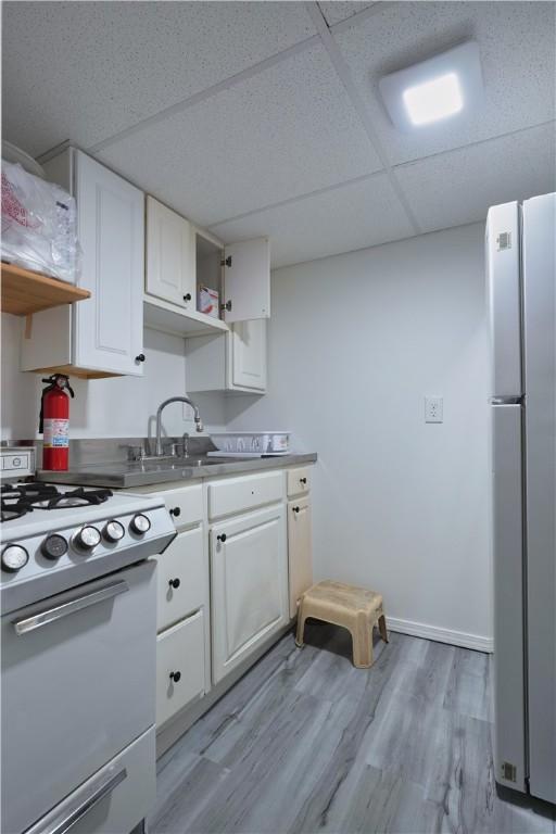 kitchen with white gas stove, white cabinets, freestanding refrigerator, and light wood-style floors