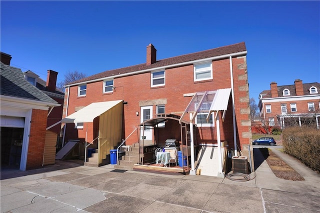 back of house with brick siding, entry steps, a chimney, and central AC