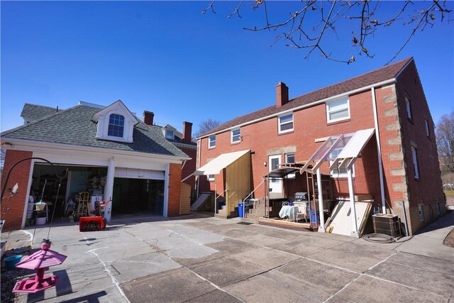 back of property featuring a garage, cooling unit, brick siding, and a shingled roof