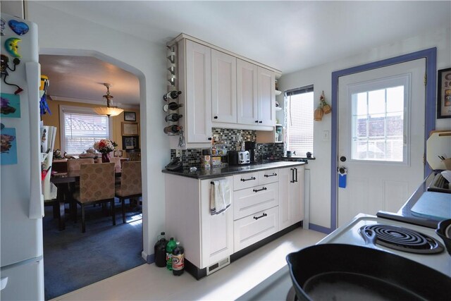 kitchen featuring arched walkways, freestanding refrigerator, decorative backsplash, white cabinetry, and dark countertops