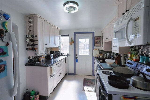 kitchen with a sink, backsplash, dark countertops, white cabinetry, and white appliances