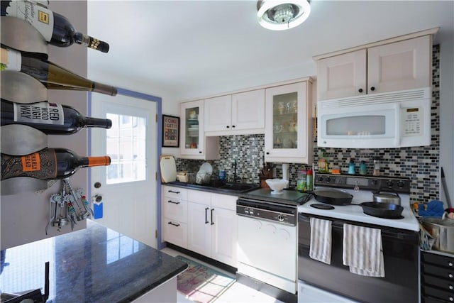 kitchen featuring dark countertops, backsplash, glass insert cabinets, white cabinets, and white appliances