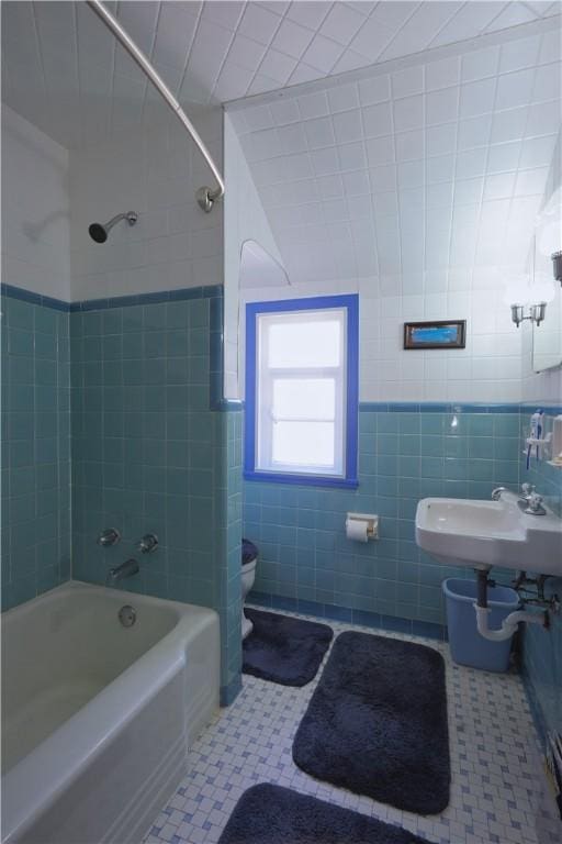 bathroom with toilet, shower / bath combination, tile patterned floors, tile walls, and a sink