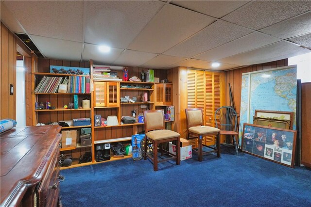 living area featuring a paneled ceiling, wooden walls, and carpet flooring