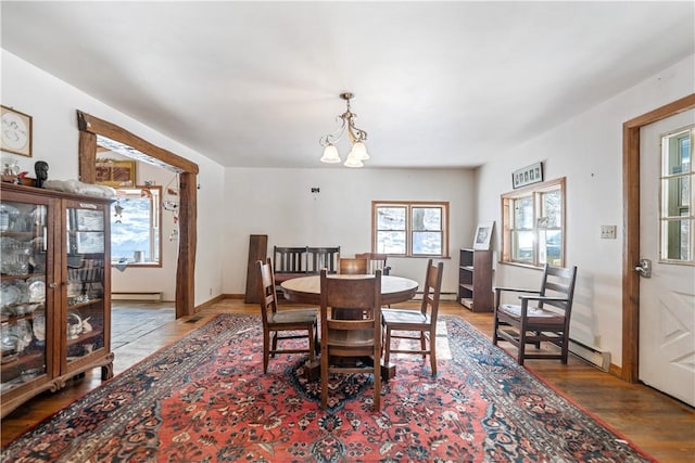 dining area featuring a baseboard heating unit, an inviting chandelier, wood finished floors, and baseboards