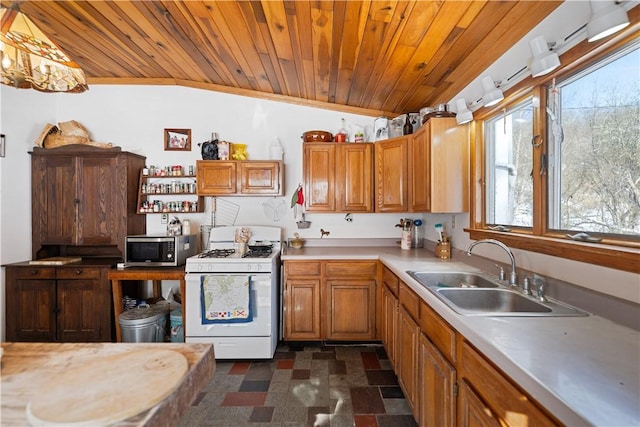 kitchen with stainless steel microwave, light countertops, vaulted ceiling, white gas range oven, and a sink