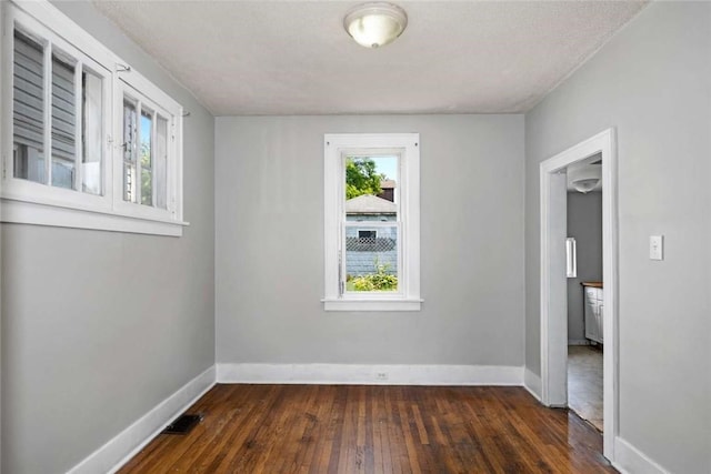 empty room with dark wood finished floors, visible vents, a healthy amount of sunlight, and baseboards