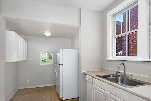 kitchen featuring a sink, freestanding refrigerator, white cabinets, light countertops, and baseboards