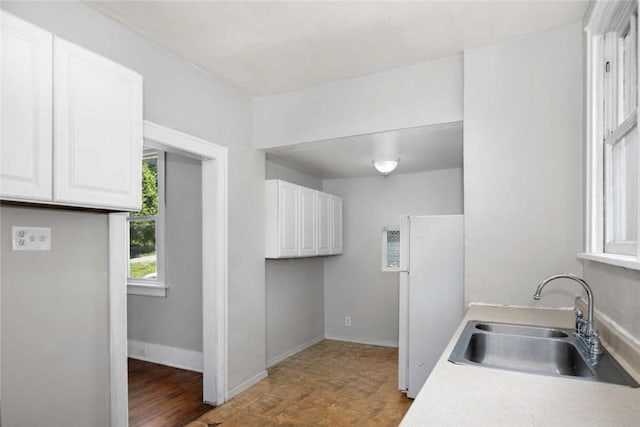 kitchen featuring white cabinets, light countertops, freestanding refrigerator, and a sink