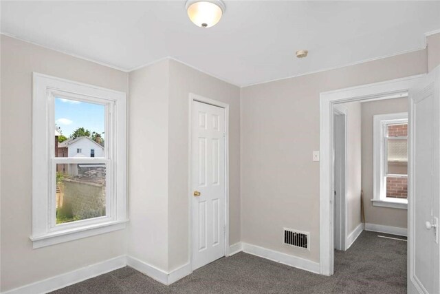 unfurnished bedroom featuring a closet, visible vents, dark carpet, and baseboards