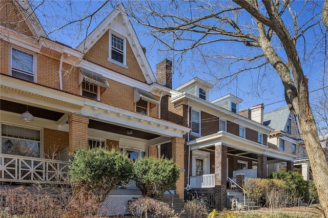 view of front of house featuring a porch, brick siding, and a chimney