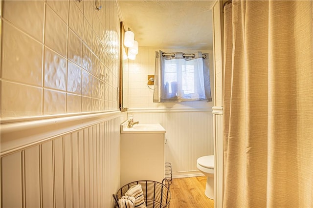 full bath featuring a wainscoted wall, toilet, vanity, and wood finished floors