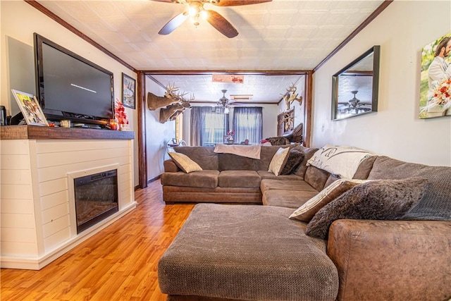 living room featuring a glass covered fireplace, wood finished floors, crown molding, and ceiling fan