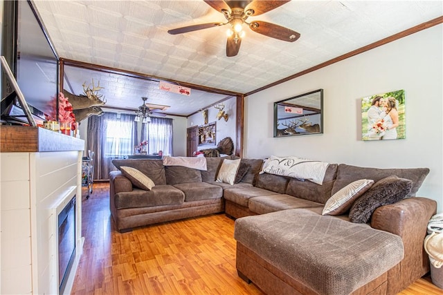 living room featuring a ceiling fan, a fireplace, light wood finished floors, and ornamental molding