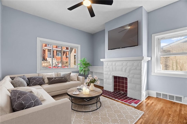 living room featuring visible vents, baseboards, a fireplace, wood finished floors, and a ceiling fan