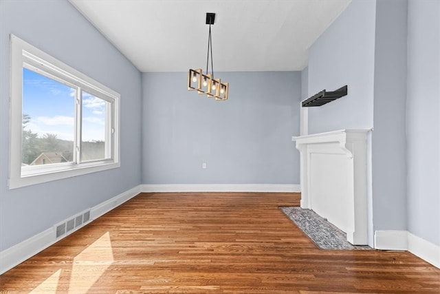 unfurnished dining area featuring a notable chandelier, visible vents, baseboards, and wood finished floors