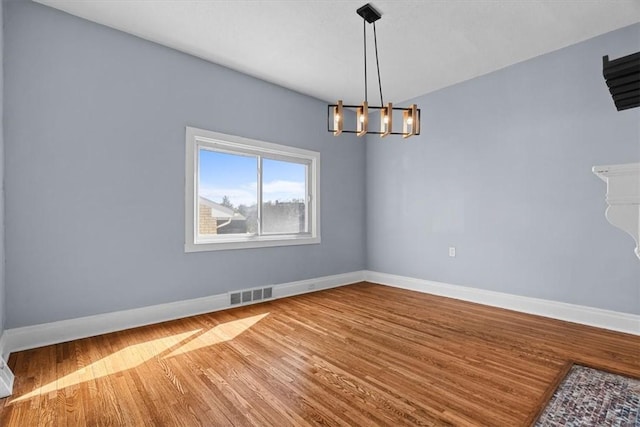 spare room featuring an inviting chandelier, wood finished floors, visible vents, and baseboards